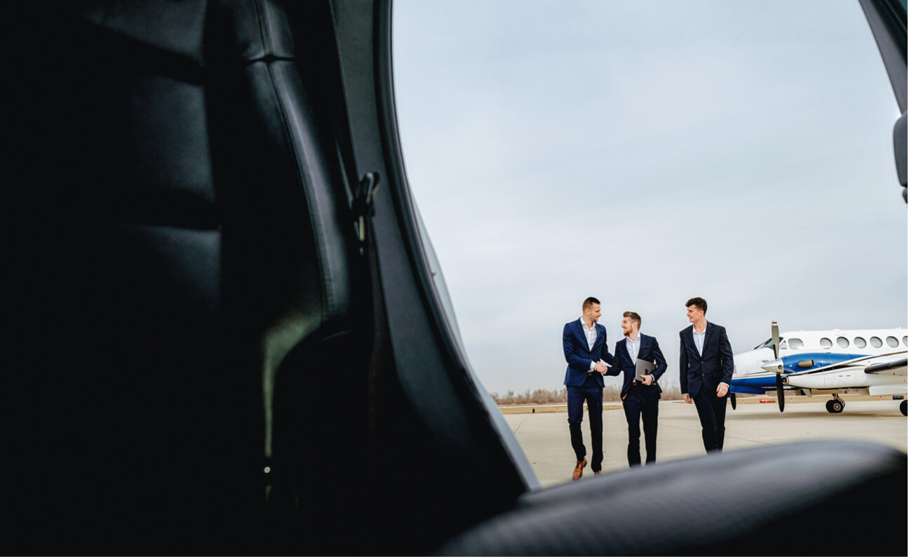 three businessmen in suits walking away from private jet towards a limo