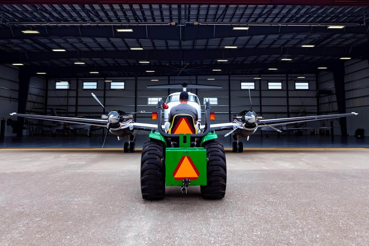 green tractor pulling charter airplane out of a hangar